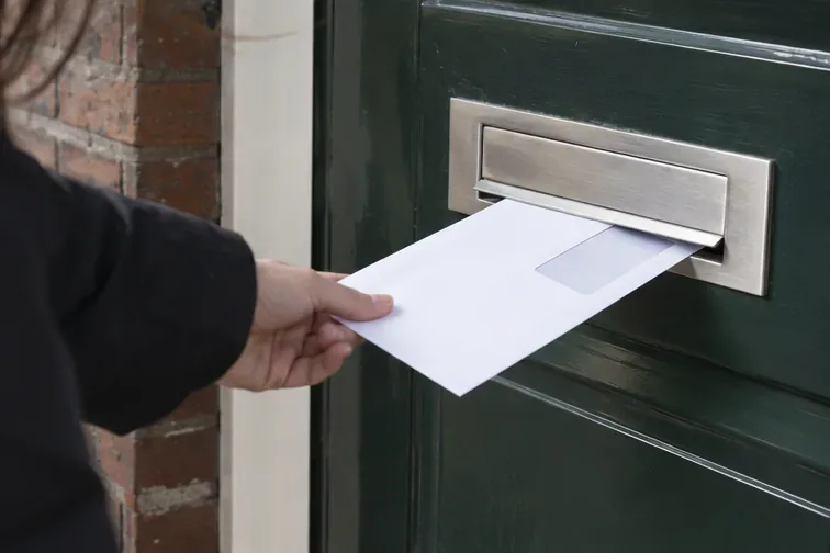 Bewoner haalt een envelop uit de brievenbus bij een Nederlandse woning