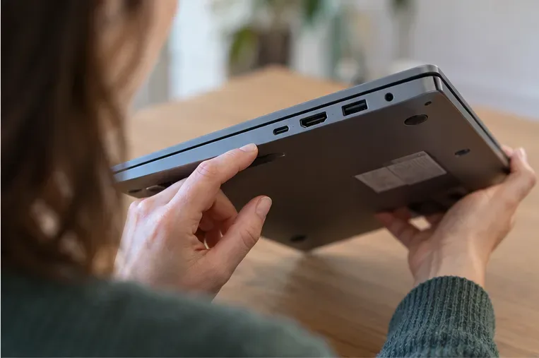 A shopper holds a laptop and checks its side ports and underside model label before comparing product listings.