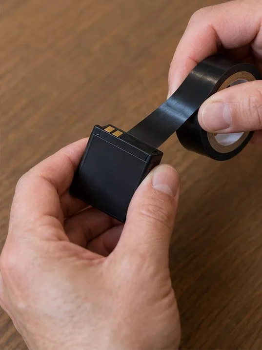 Des mains appliquent un morceau de ruban isolant sur les contacts d’une batterie amovible intacte