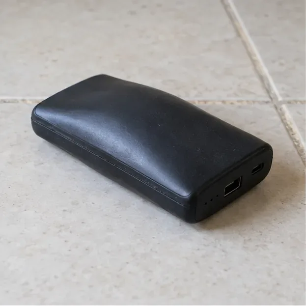 Batterie externe noire dont le boîtier est bombé, posée seule sur un carrelage clair