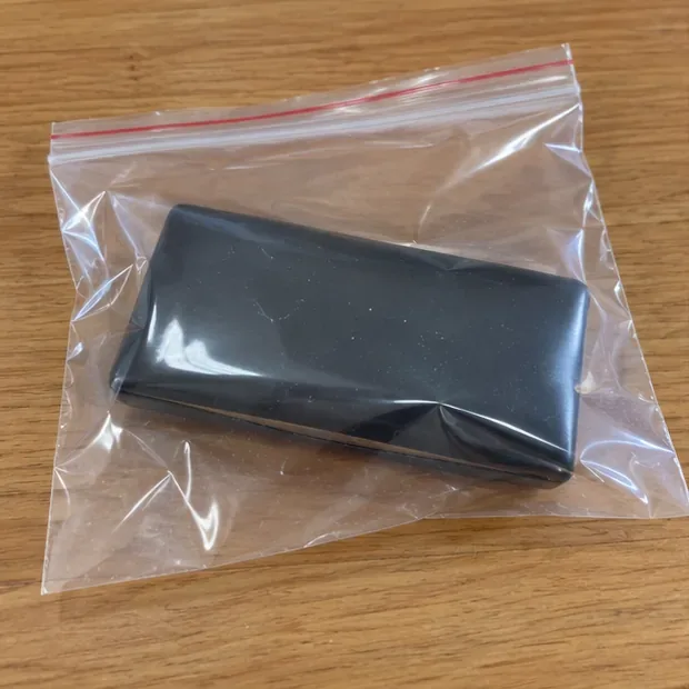 Batterie externe gonflée placée seule dans un sachet plastique transparent refermable sur une table en bois