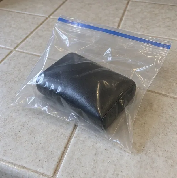 Une batterie externe noire placée seule dans un sachet transparent refermé et posée sur du carrelage.