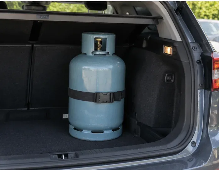 Une bouteille de gaz bleue est transportée debout dans le coffre d’une voiture et maintenue par une large sangle.