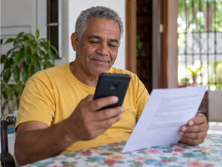 Um homem confere um documento e consulta o celular depois de enviar uma solicitação