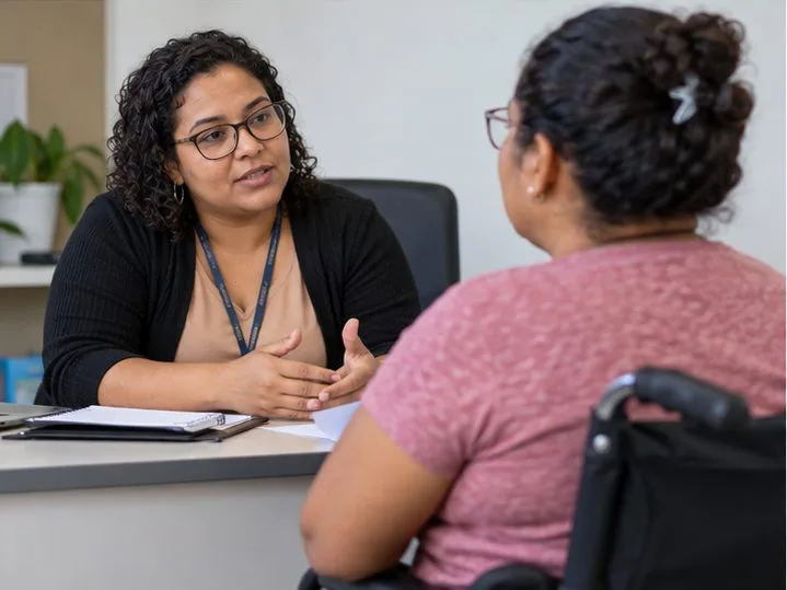 Uma assistente social conversa com uma mulher cadeirante em uma sala de atendimento