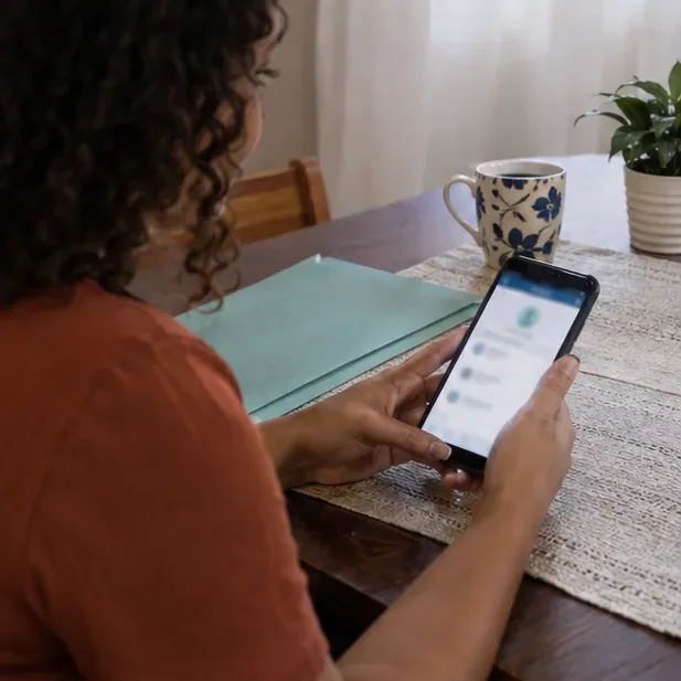 Pessoa consulta no celular uma página de situação cadastral em casa, com a tela desfocada e sem dados pessoais legíveis.
