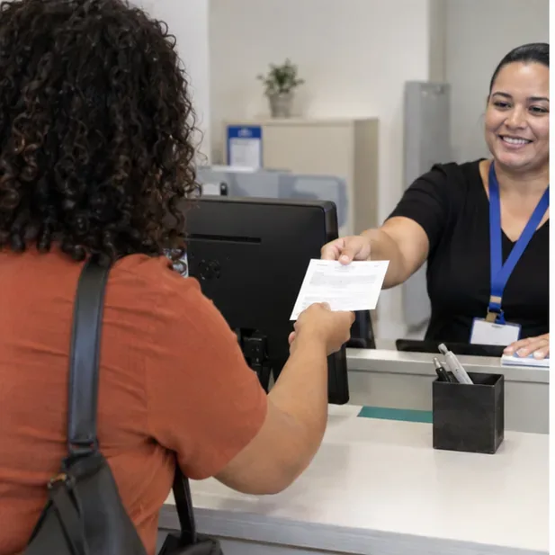 Trabalhadora entrega um documento de protocolo a uma pessoa no balcão de atendimento.
