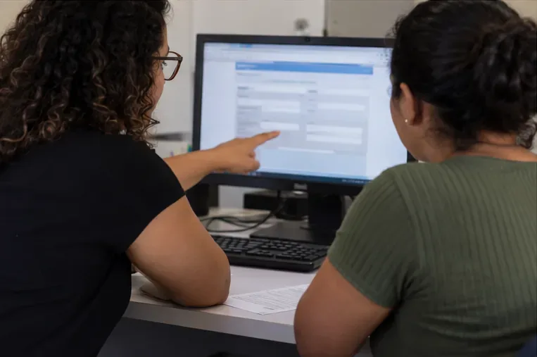 Atendente e cidadã observando juntas um formulário eletrônico em um computador durante atendimento presencial.