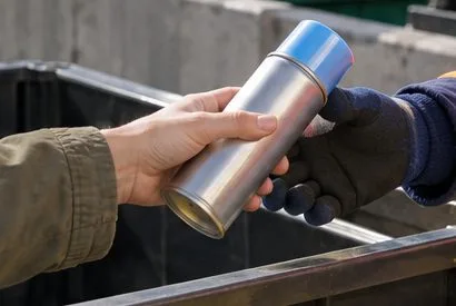 Una persona passa una bomboletta spray integra a un addetto con guanti in un’area di raccolta.
