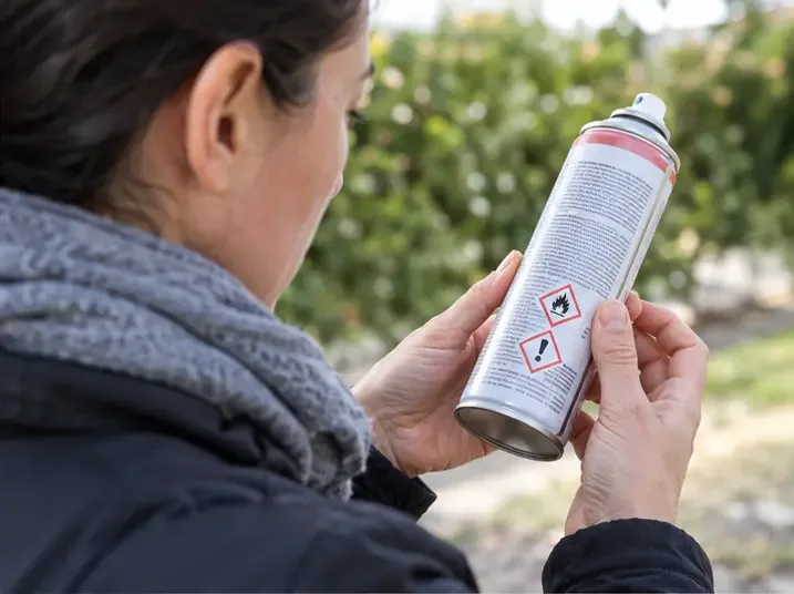 Persona che legge i pittogrammi di pericolo sull'etichetta di una bomboletta spray all'aperto