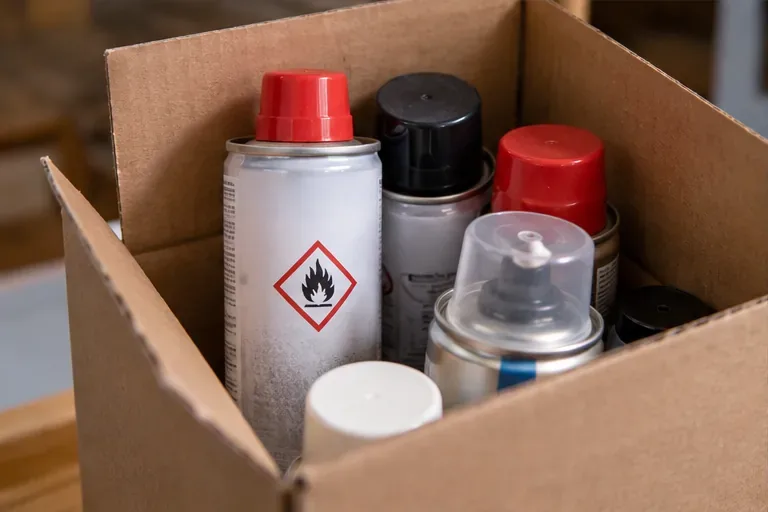 Bombolette spray con pittogramma di infiammabilità sistemate verticalmente in una scatola di cartone per il trasporto