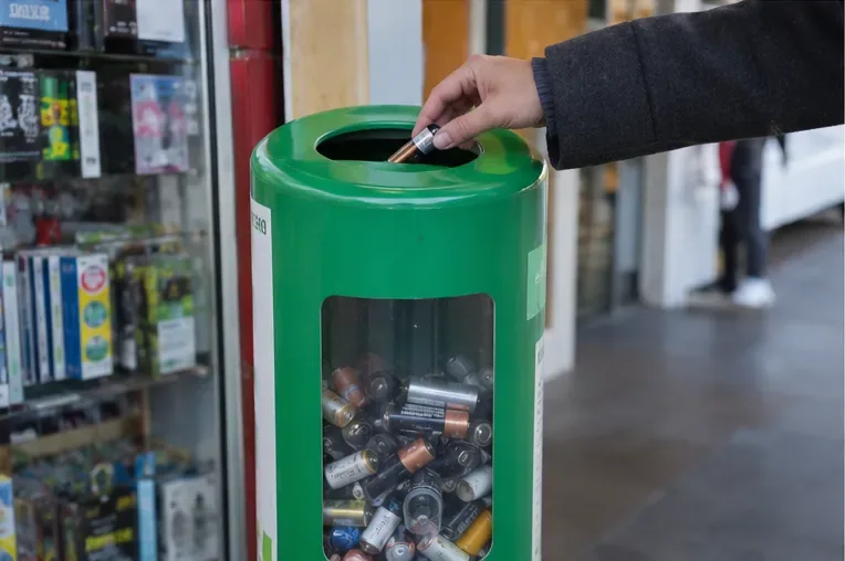 Una mano introduce pile scariche nell’apertura di un contenitore dedicato alla raccolta delle batterie usate
