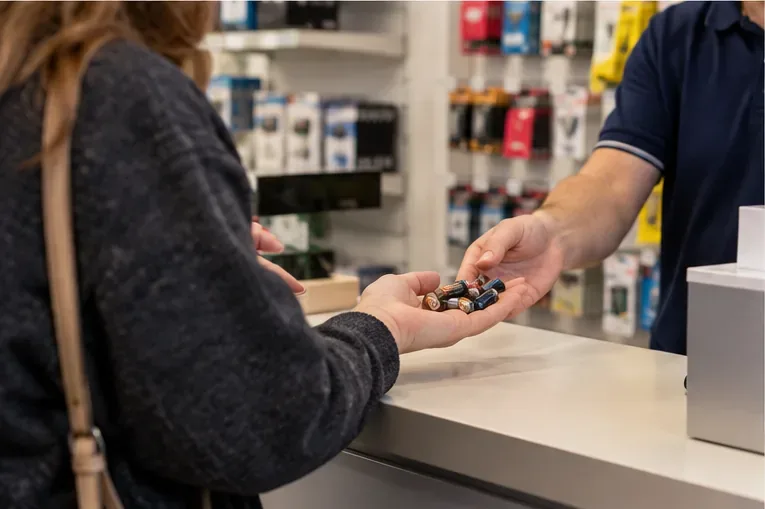 Cliente che consegna alcune pile usate al banco di un negozio che vende prodotti elettrici