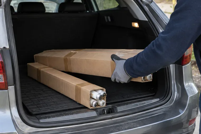 Tubi fluorescenti inseriti in lunghe scatole di cartone e sistemati nel bagagliaio di un'auto