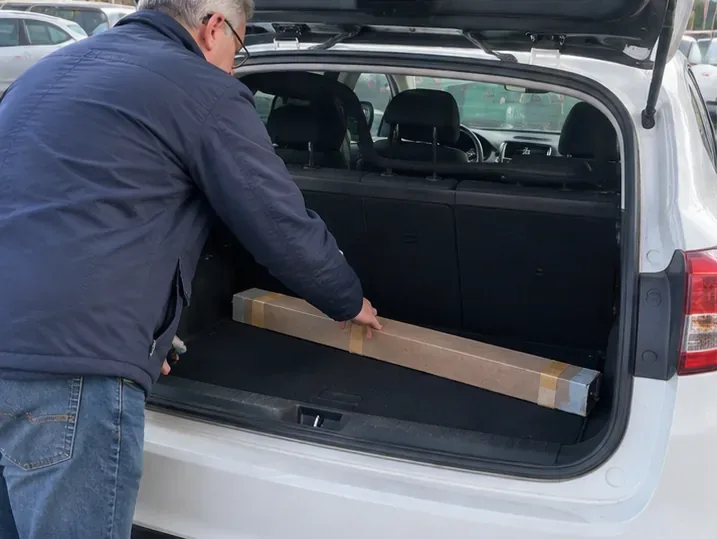 Una persona sistema nel bagagliaio di un’auto una confezione lunga di cartone contenente un tubo fluorescente protetto