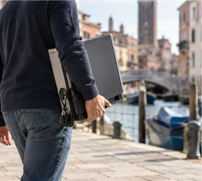 Persona che trasporta un vecchio computer lungo una fondamenta veneziana verso un punto di raccolta