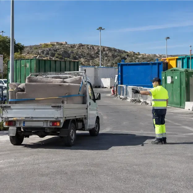 Piccolo veicolo con un divano fissato sul pianale che arriva in un ecocentro con contenitori e un operatore che indica il percorso