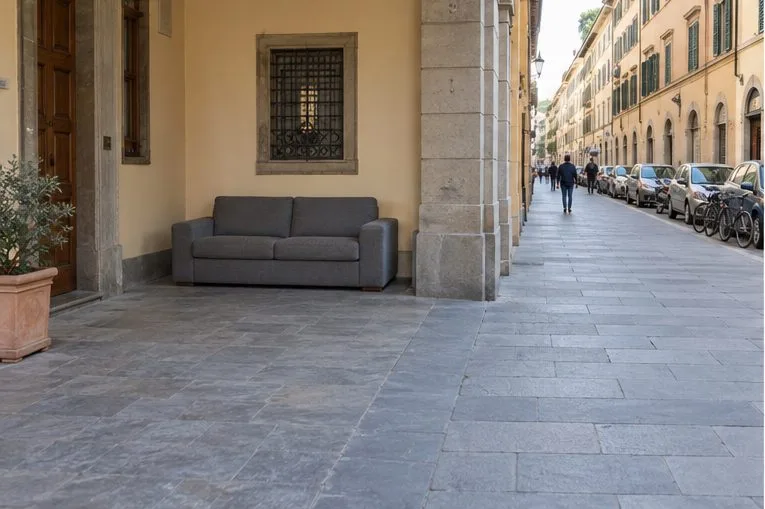 Un divano grigio è appoggiato vicino a una facciata lungo un ampio marciapiede.