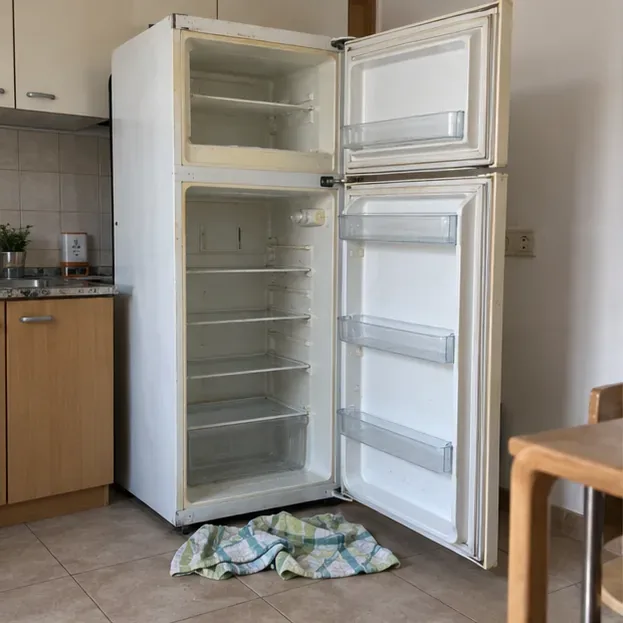 Vecchio frigorifero vuoto con porte aperte in cucina e panno sul pavimento durante la preparazione allo smaltimento