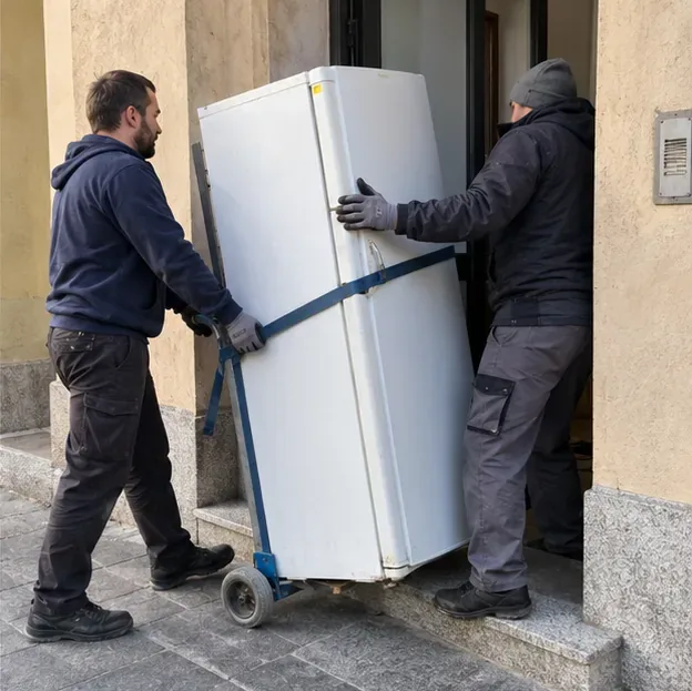 Due addetti movimentano un frigorifero verticale con un carrello e una cinghia all'ingresso di un edificio