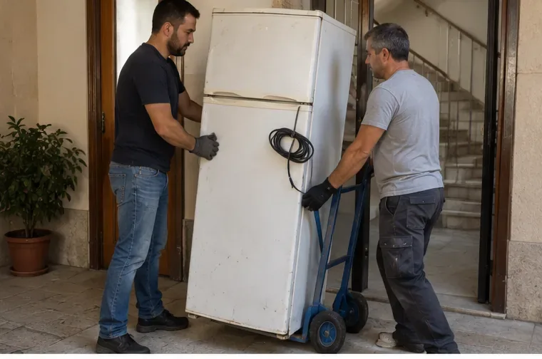 Due persone spostano un vecchio frigorifero con un carrello a due ruote attraverso un ingresso