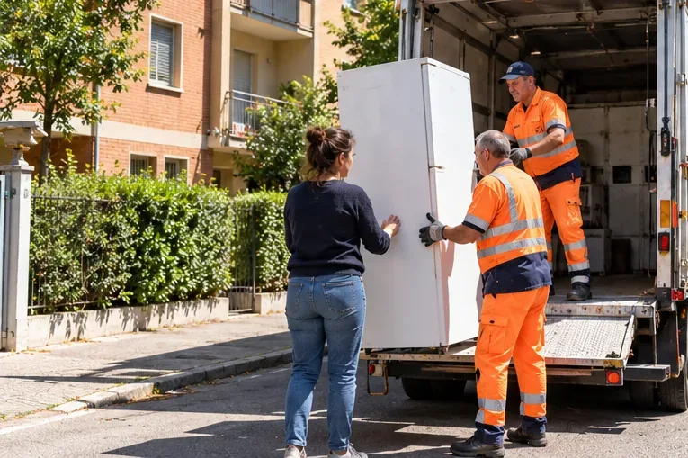 Operatori addetti alla raccolta caricano un frigorifero integro su un automezzo mentre la proprietaria assiste
