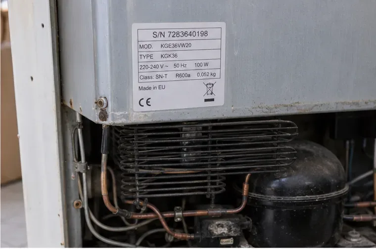 Dettaglio della targhetta tecnica e del gruppo compressore sul retro di un vecchio frigorifero.