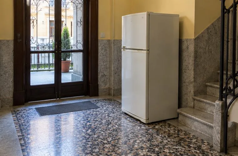 Un frigorifero bianco è collocato in un ingresso interno, lontano dalla carreggiata e dai cassonetti stradali.