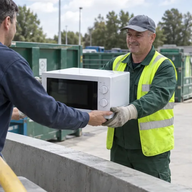 Un addetto in abbigliamento da lavoro riceve un microonde intero da un cittadino in un centro di raccolta.