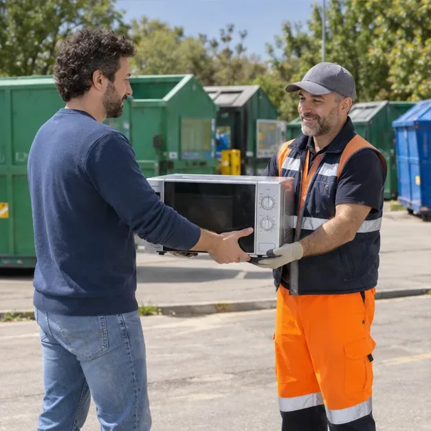 Un addetto in abbigliamento da lavoro riceve un microonde da un cittadino in un centro di raccolta con contenitori per materiali diversi