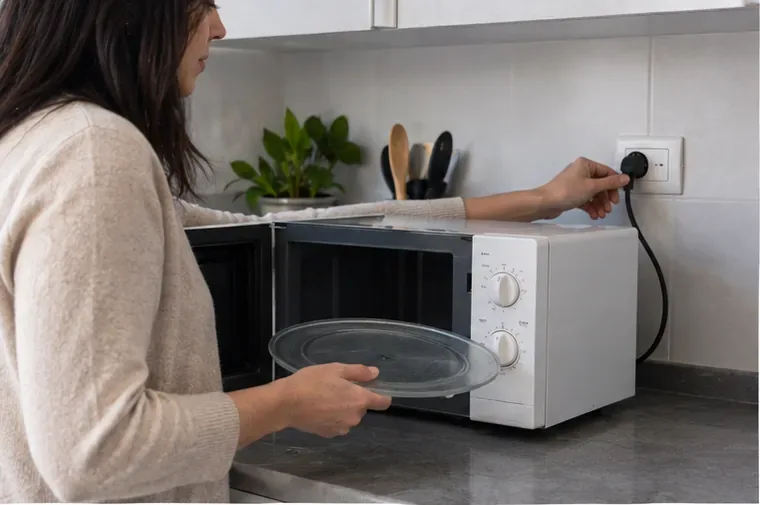 Una persona scollega un forno a microonde dalla presa e rimuove il piatto in vetro prima del conferimento