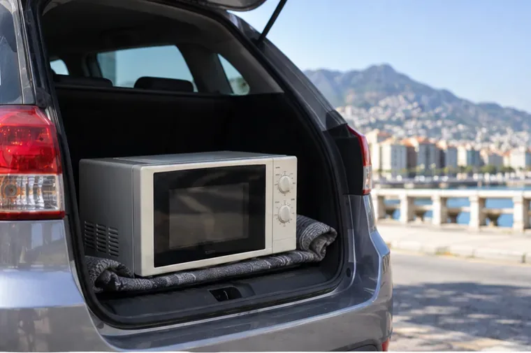 Un forno a microonde appoggiato in modo stabile nel bagagliaio di un'auto per il trasporto al centro di raccolta