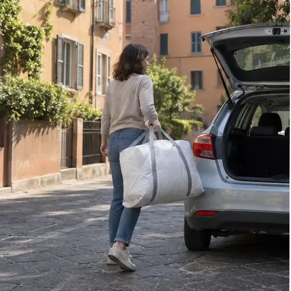 Una donna trasporta una custodia contenente un piumone verso il bagagliaio di una piccola auto in una strada di Bologna