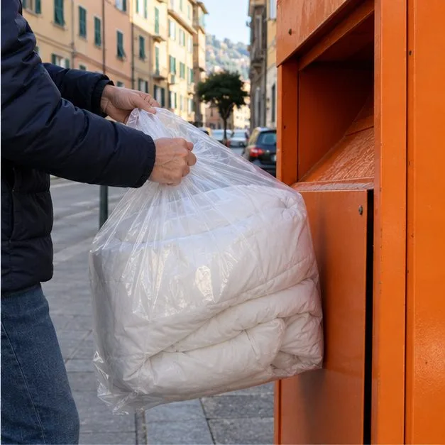 Una persona inserisce un sacco chiuso con un piumone in un contenitore tessile arancione