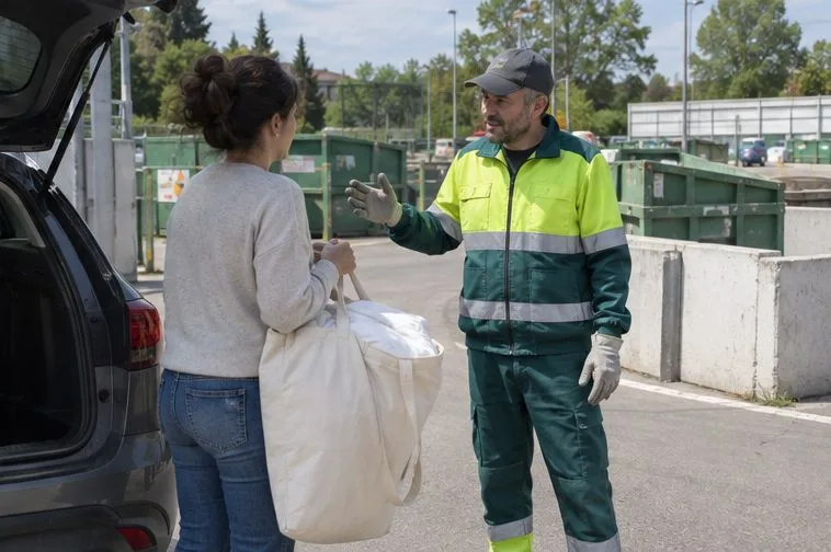 Una cittadina chiede indicazioni a un addetto all’ingresso di un centro di raccolta prima di scaricare un sacco voluminoso