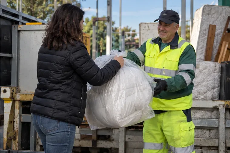 Una donna consegna un piumone imballato a un operatore della raccolta vicino a un mezzo per rifiuti ingombranti