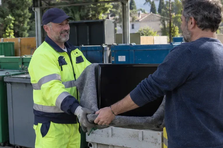 Operatore con abbigliamento ad alta visibilità riceve un televisore protetto presso un’area di raccolta con contenitori