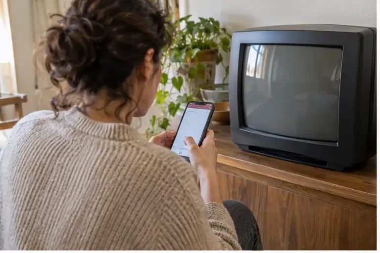 Una persona consulta le informazioni sul conferimento dei rifiuti su uno smartphone accanto a un vecchio televisore