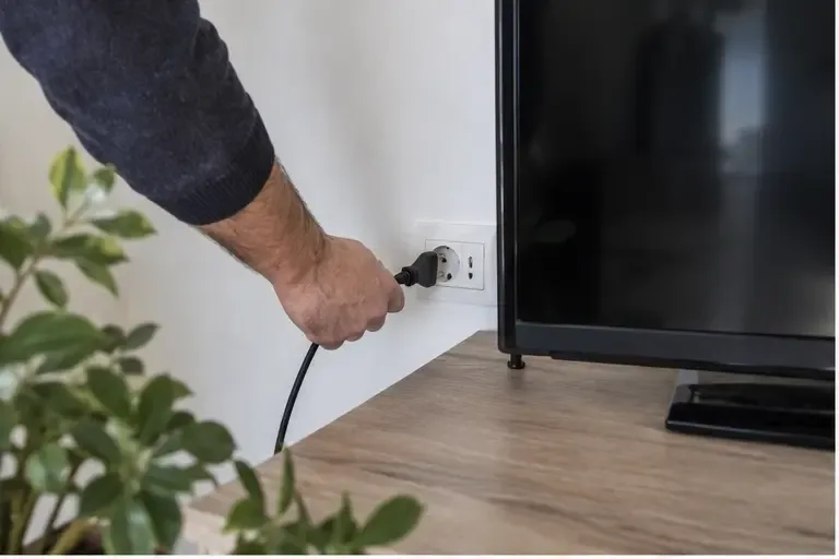 Una persona scollega il cavo di alimentazione di un televisore dalla presa a muro