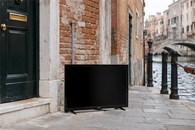 Televisore appoggiato vicino a un ingresso lungo una calle veneziana accanto a un canale