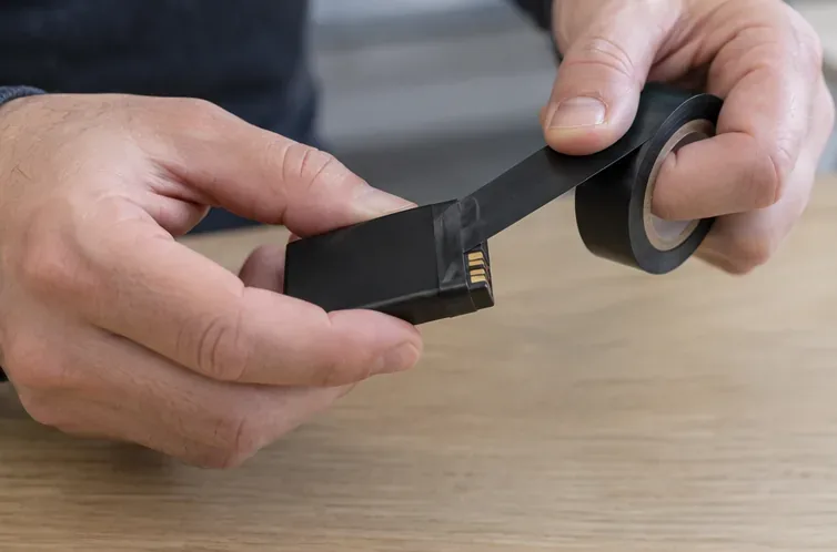 Una persona applica nastro isolante sui contatti metallici di una batteria al litio integra
