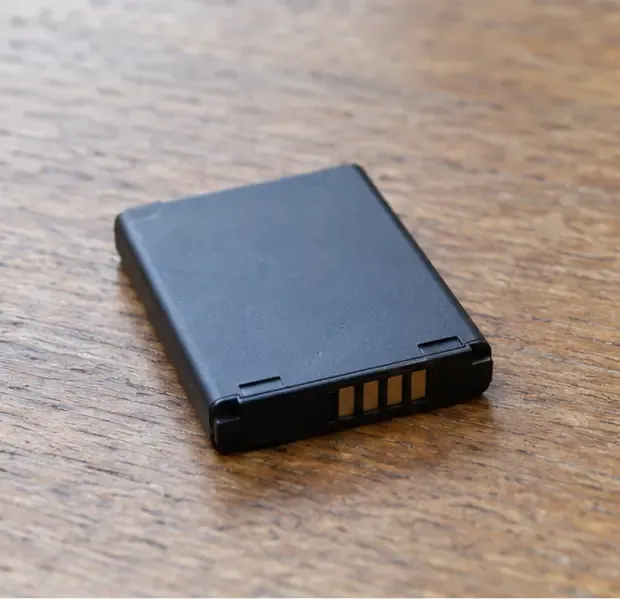 Piccola batteria al litio integra appoggiata su un tavolo di legno, con i contatti metallici visibili