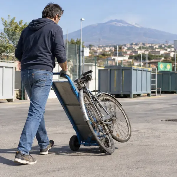 Una persona trasporta una vecchia bicicletta su un carrello verso un centro comunale di raccolta