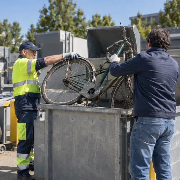 Un operatore indica il contenitore per i metalli mentre una vecchia bicicletta viene conferita in una ricicleria