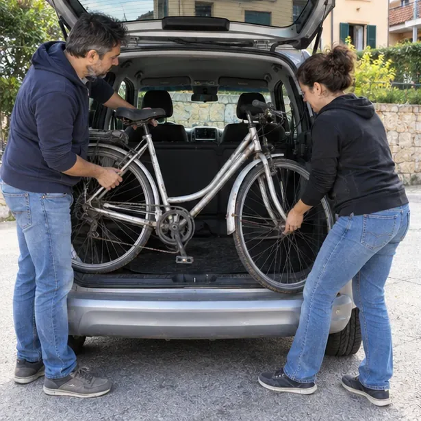 Due persone caricano con cautela una bicicletta nel bagagliaio di un’auto