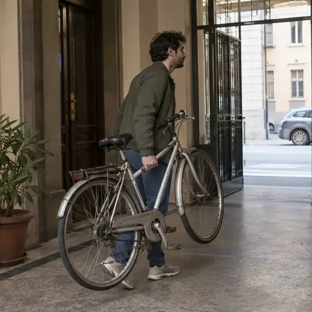 Una persona trasporta una bicicletta tradizionale attraverso l’ingresso di un edificio torinese, tenendola dal telaio