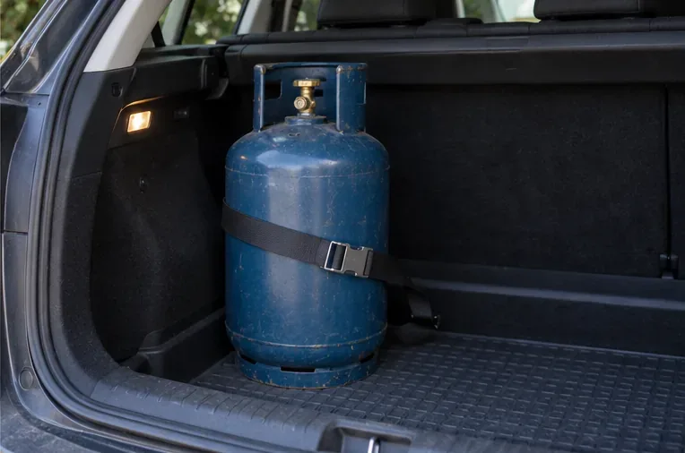 Una bombola GPL blu è fissata in posizione verticale nel vano bagagli di un'automobile con una cinghia che ne limita i movimenti.