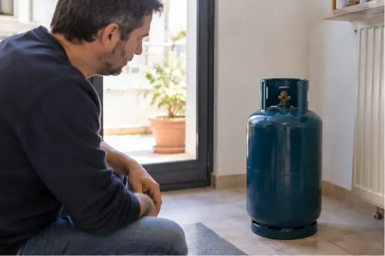 Una bombola GPL blu tenuta in posizione verticale in un ambiente domestico mentre una persona la osserva a distanza
