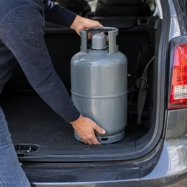 Persona che colloca verticalmente una bombola GPL integra e protetta nel vano bagagli di un’auto