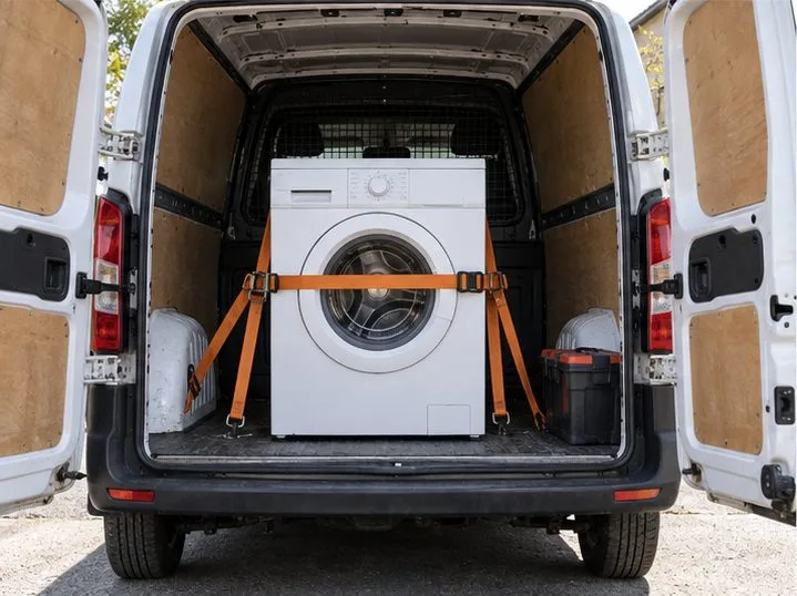 Una lavatrice è trasportata in verticale e fissata con cinghie all’interno di un furgone.